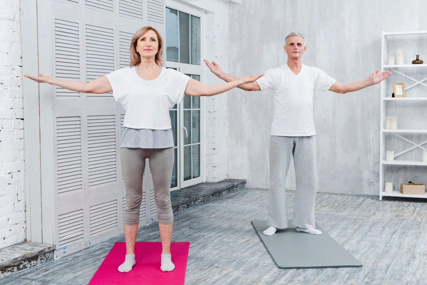 couple-performing-yoga-by-outstretching-arms-standing-yoga-mat_23-2148097421