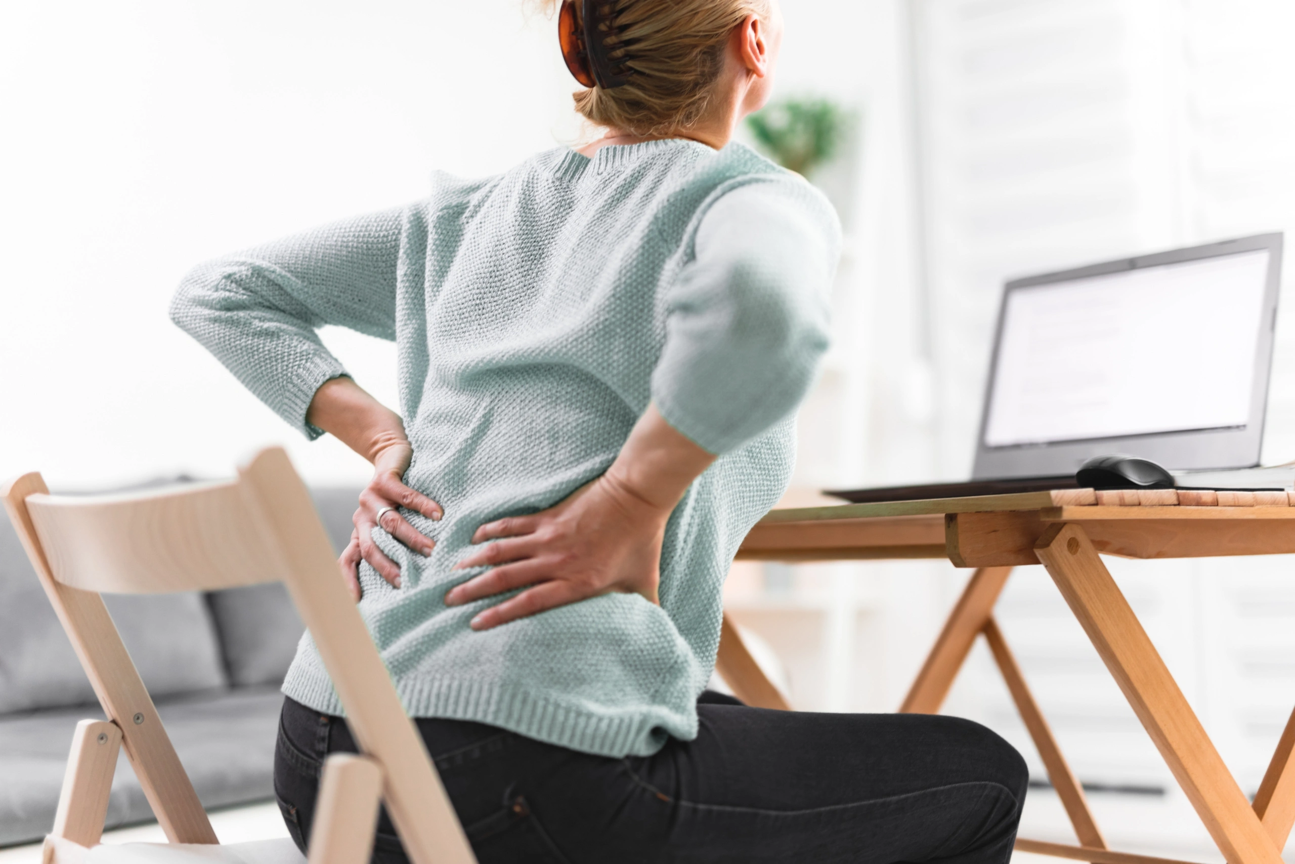 Woman working on a laptop and having back, hip, spine pain.